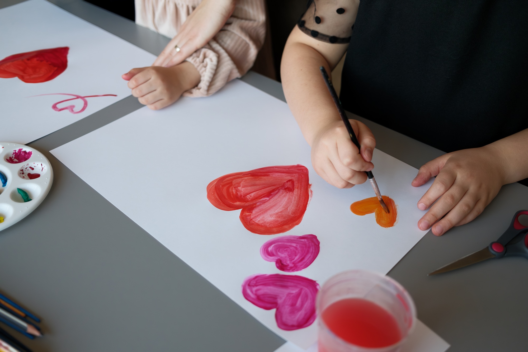 Children creating colorful heart paintings with watercolors at a crafting table