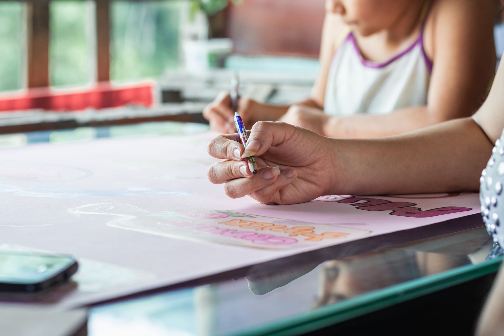 Closeup shot of a young Latina mother helping her child color a poster for school