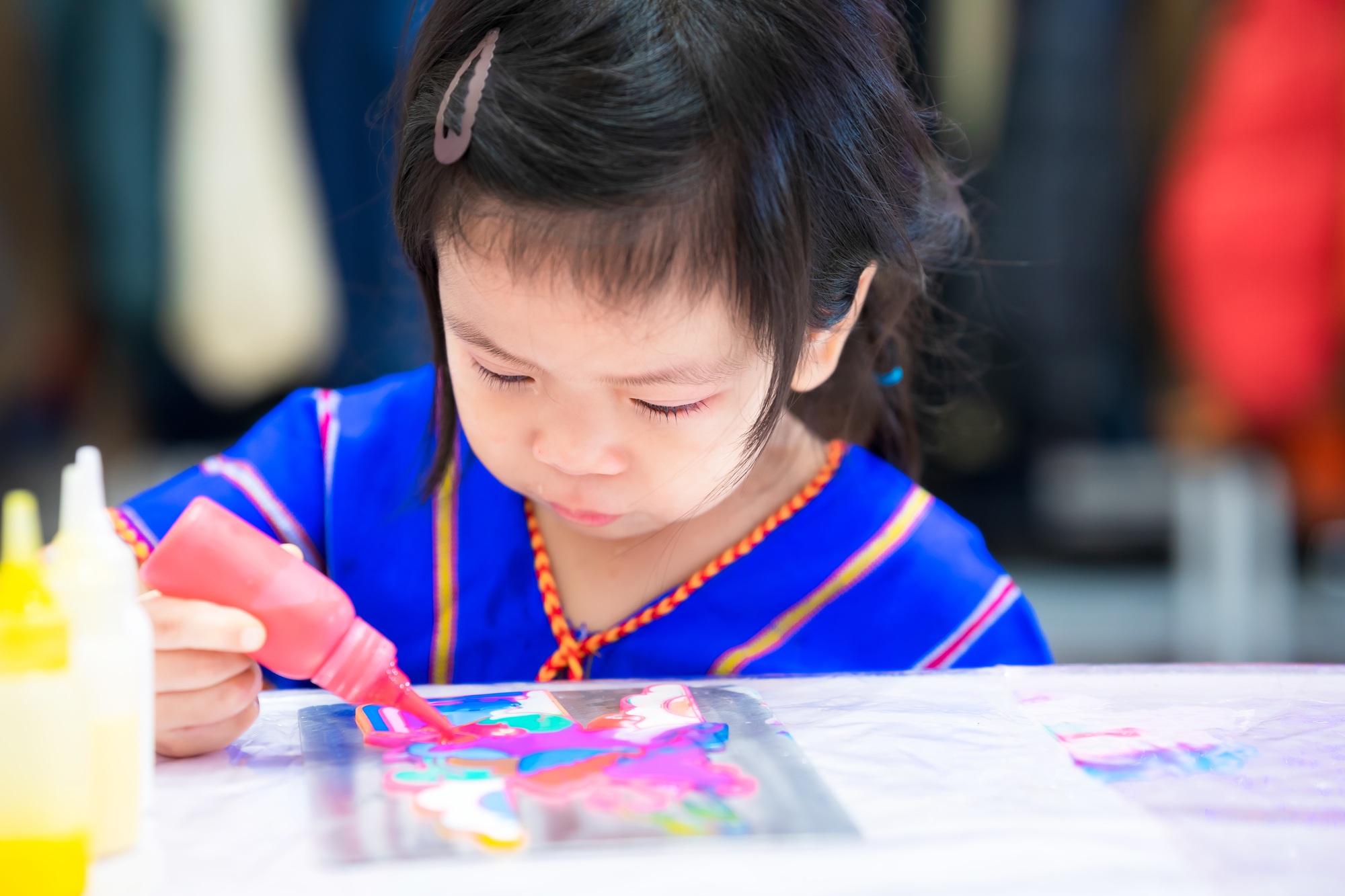 Girl play magic color water drops onto the rainbow cartoon mold. Children do table art.