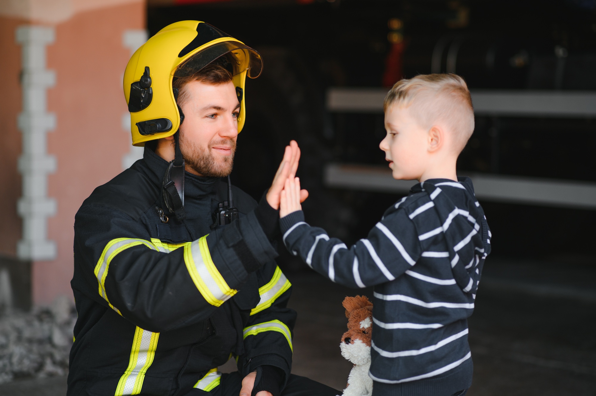 Portrait of rescued little boy with firefighter man standing near fire truck.